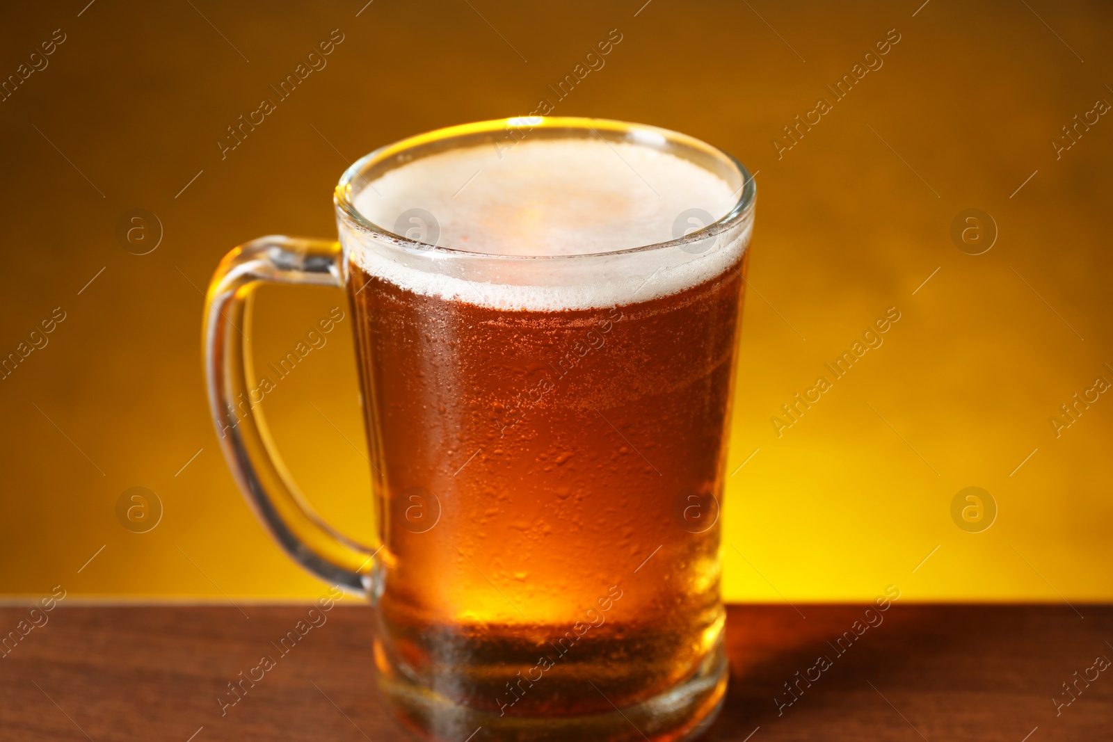 Photo of Mug with fresh beer on wooden table against dark background, closeup