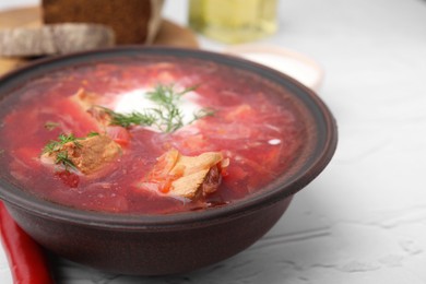 Photo of Tasty borscht with sour cream in bowl on white textured table, closeup