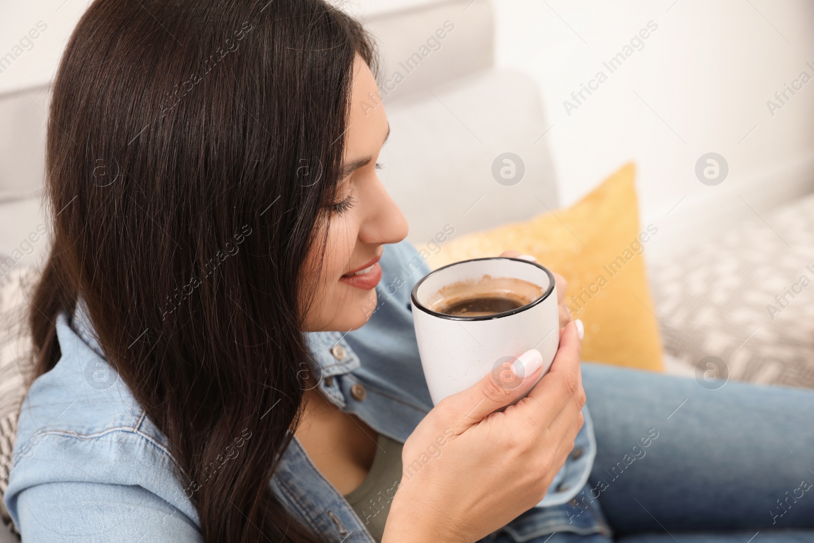 Photo of Young woman with cup of drink relaxing on couch at home