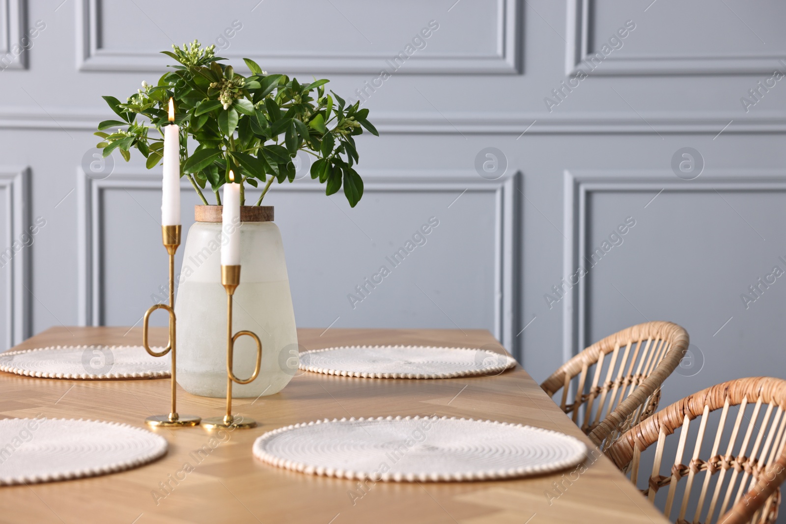 Photo of Vase with green branches and burning candles on wooden table in stylish dining room