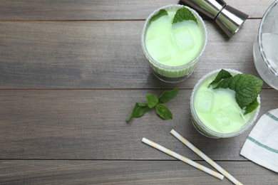 Photo of Delicious mint liqueur with green leaves and ice cubes on grey wooden table, flat lay. Space for text