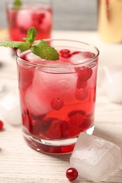 Photo of Tasty cranberry cocktail with ice cubes in glass on wooden table