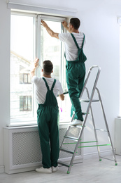 Professional workers tinting window with foil indoors