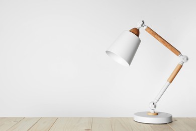 Stylish modern desk lamp on wooden table, space for text