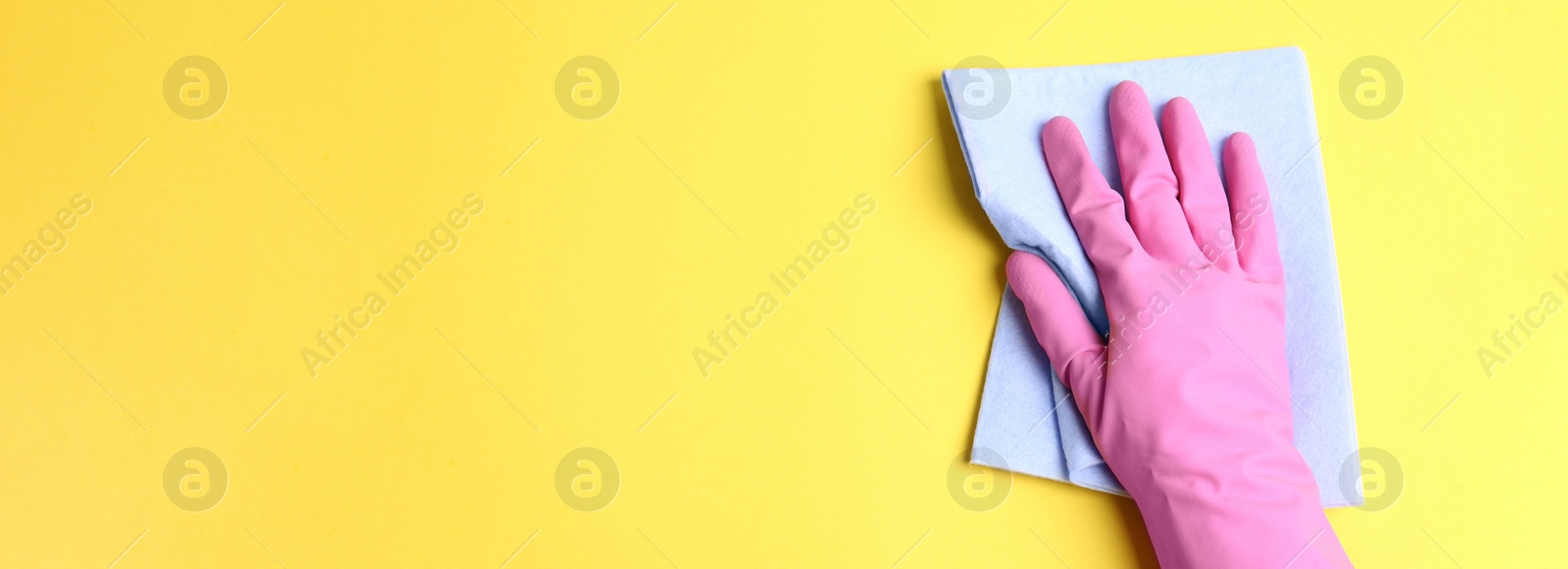 Image of Closeup view of person in rubber glove cleaning yellow surface with rag, space for text. Banner design