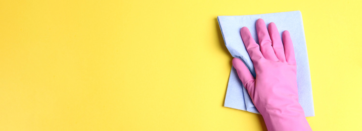 Image of Closeup view of person in rubber glove cleaning yellow surface with rag, space for text. Banner design