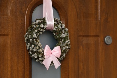 Photo of Wreath made of beautiful willow branches and pink bow on wooden door