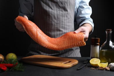 Photo of Man with raw salmon fillet at black table, closeup