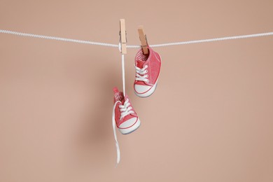 Photo of Cute small baby shoes hanging on washing line against brown background
