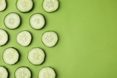 Fresh slices of cucumbers on green background, top view. Space for text