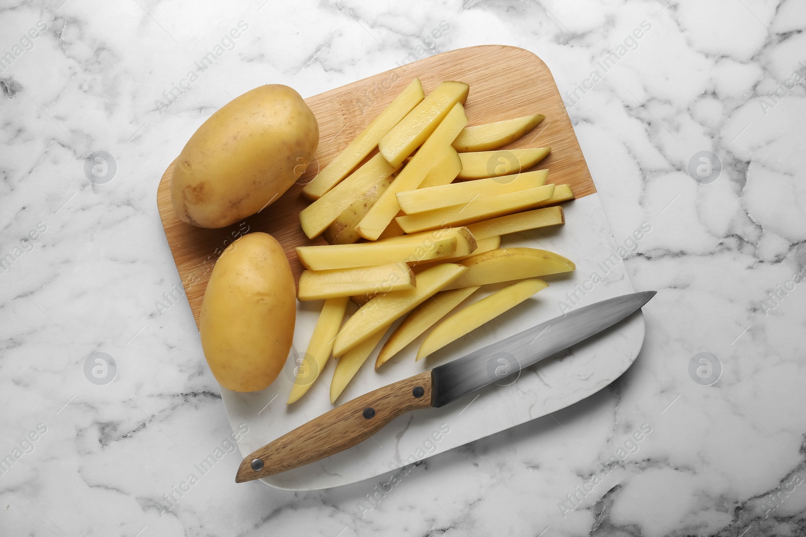 Photo of Whole and cut raw potatoes with knife on white marble table, top view. Cooking delicious French fries