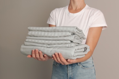 Photo of Woman holding stack of clean bed linens on beige background