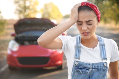 Stressed woman having headache near broken car outdoors