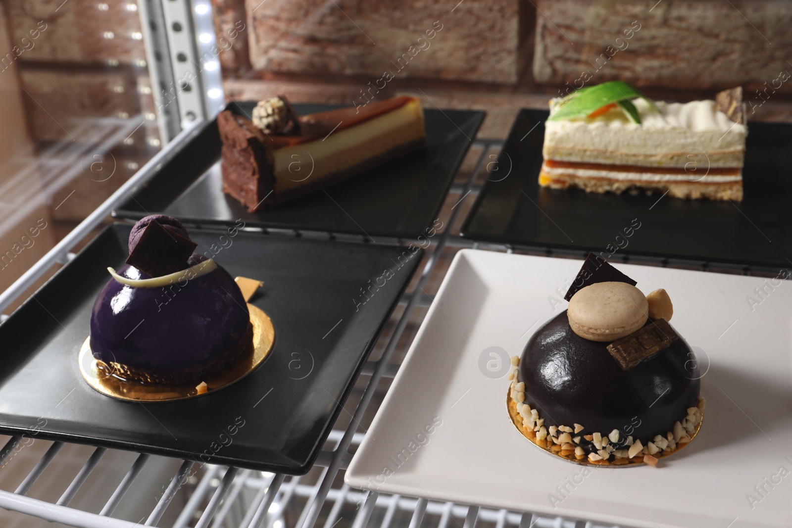 Photo of Display case with different delicious desserts on shelf in cafe, closeup