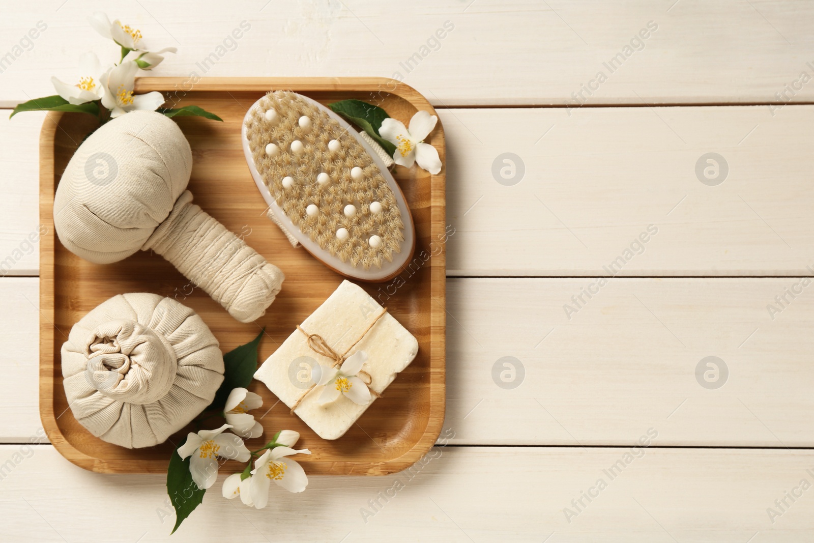 Photo of Beautiful jasmine flowers, herbal bags, brush and soap bar on white wooden table, top view. Space for text