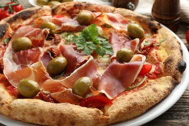 Photo of Tasty pizza with cured ham, olives, sun-dried tomato and parsley on table, closeup