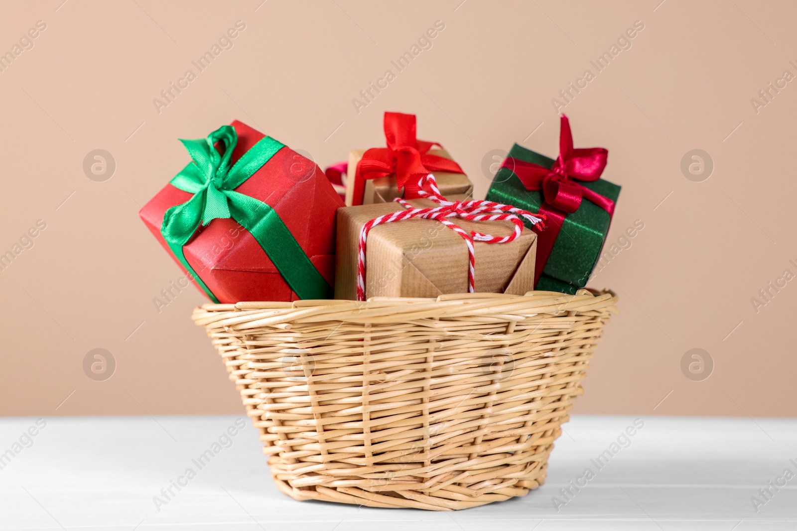 Photo of Wicker basket full of gift boxes on white wooden table against beige background