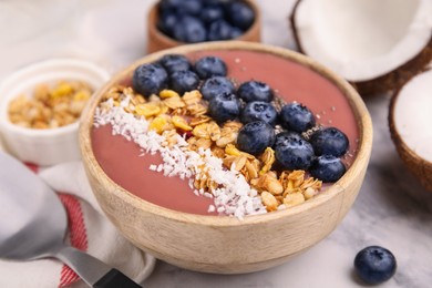 Bowl of delicious fruit smoothie with fresh blueberries, granola and coconut flakes on white marble table, closeup