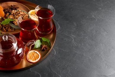 Photo of Tray with glasses of traditional Turkish tea, pot and ingredients on black table. Space for text