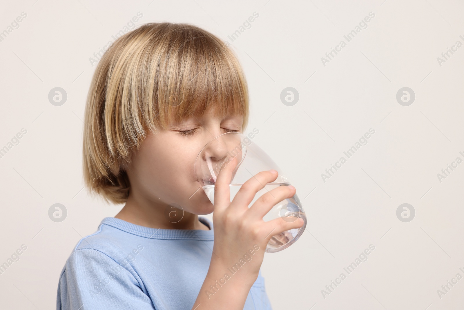 Photo of Cute little boy drinking fresh water from glass on white background. Space for text