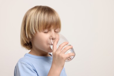 Photo of Cute little boy drinking fresh water from glass on white background. Space for text