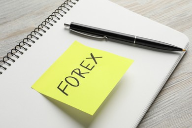 Photo of Sticky note with word Forex, notebook and pen on wooden table, closeup