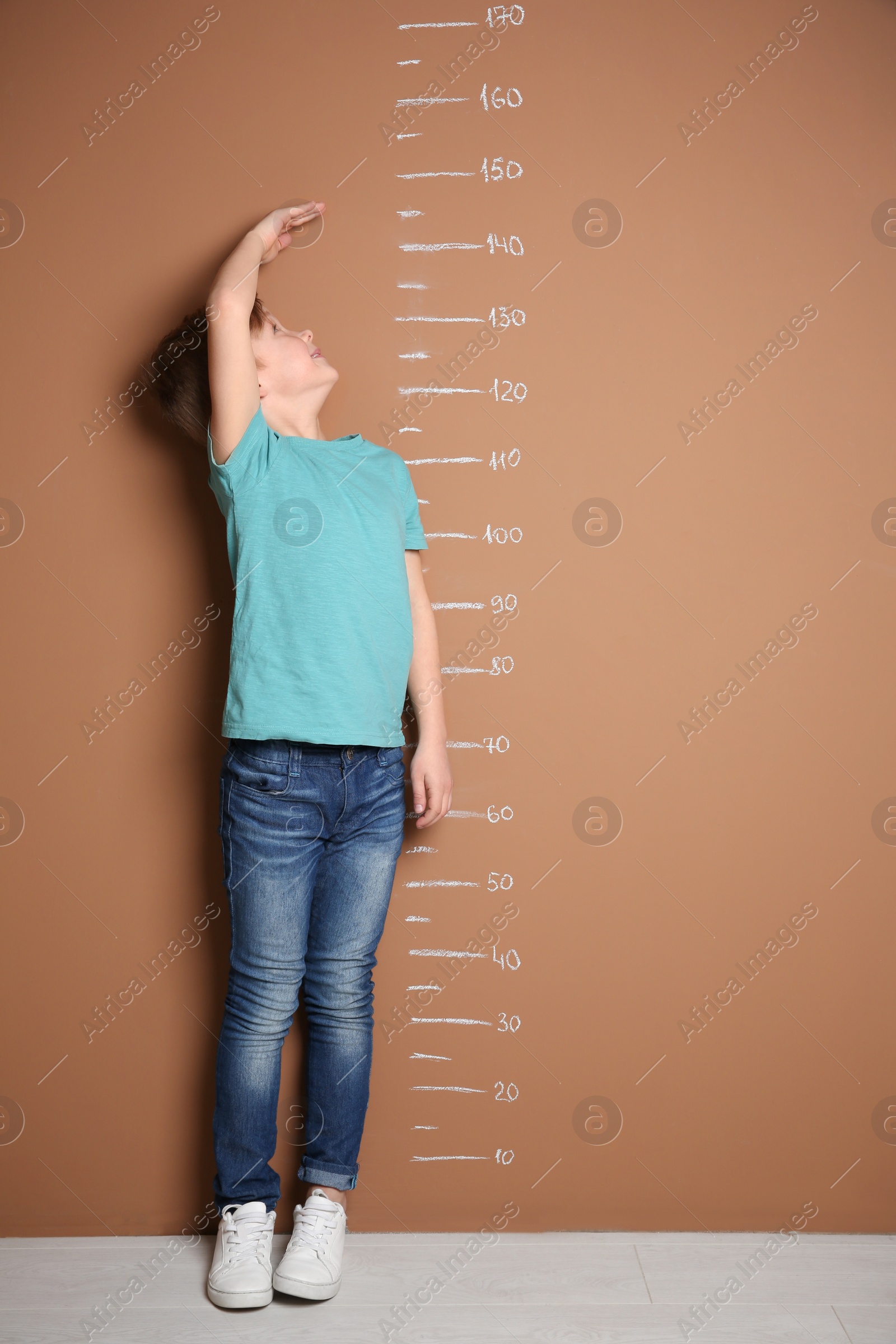 Photo of Little boy measuring his height near color wall