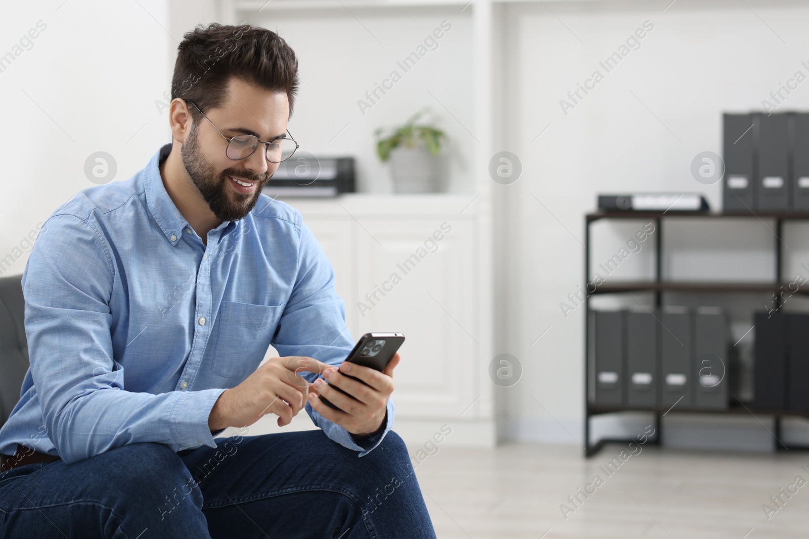 Photo of Handsome young man using smartphone in office, space for text