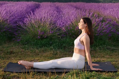 Photo of Beautiful woman practicing yoga near blooming lavender outdoors. Space for text