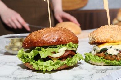 Woman cutting bun at white marble table, focus on delicious vegetarian burgers