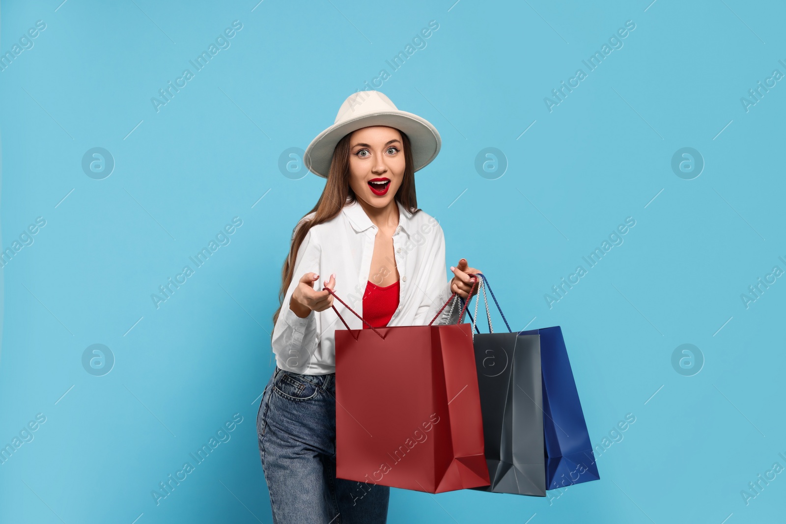 Photo of Excited young woman with shopping bags on light blue background