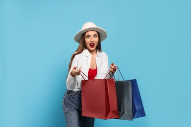 Excited young woman with shopping bags on light blue background