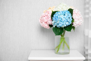 Photo of Beautiful hydrangea flowers in vase on white bedside table near light gray wall. Space for text