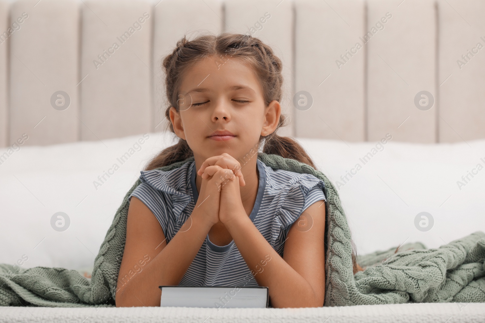 Photo of Cute little girl praying over Bible in bedroom