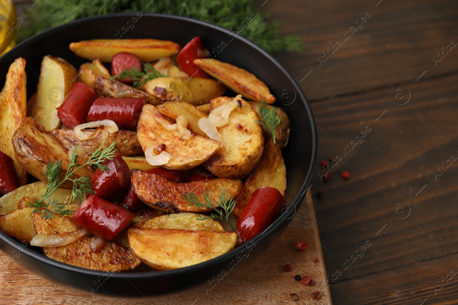 Photo of Delicious baked potato with thin dry smoked sausages, onion and dill in bowl on wooden table, closeup