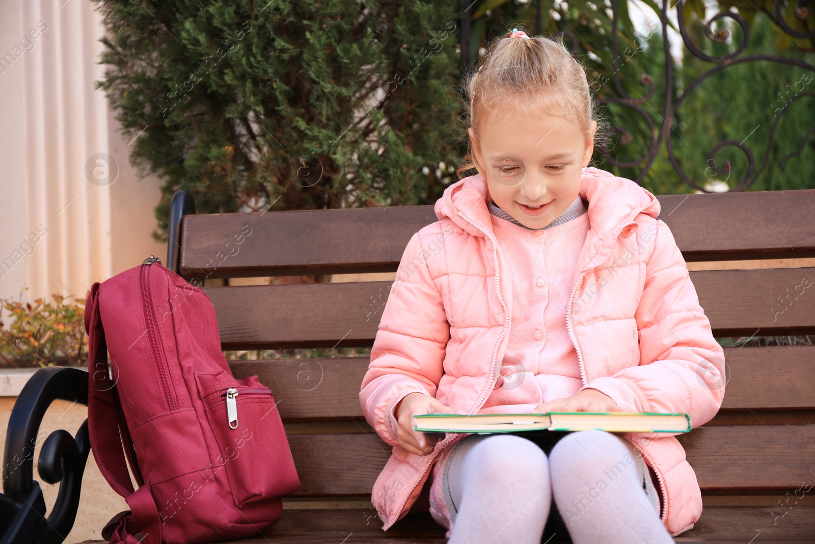 Photo of Cute little girl with backpack and books on bench outdoors