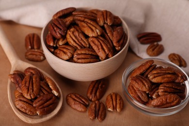 Photo of Bowls and spoon with tasty pecan nuts on wooden table, closeup