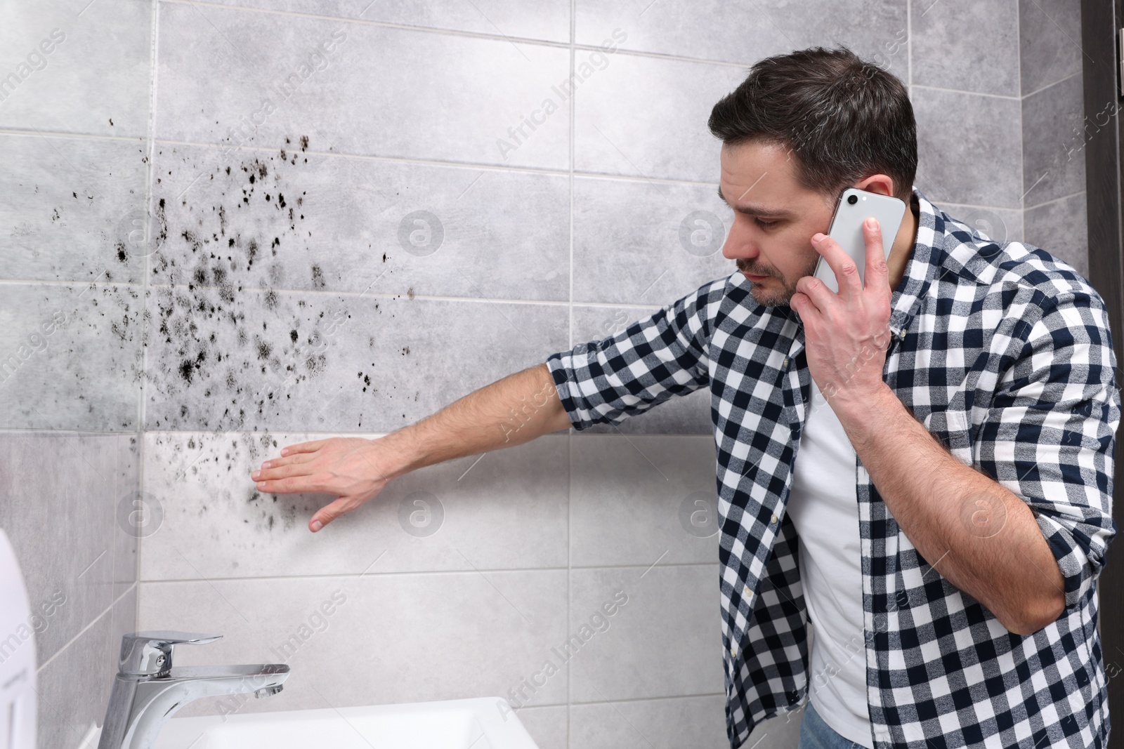 Image of Mold removal service. Man talking on phone and looking at affected walls in bathroom