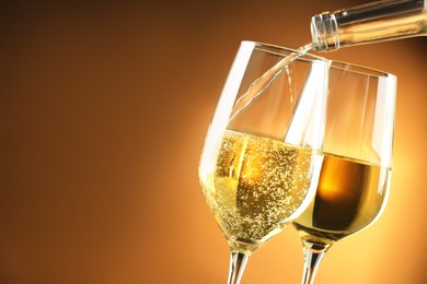 Pouring tasty aromatic wine in glass on brown background, closeup. Space for text