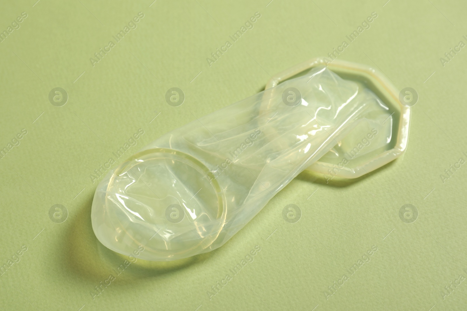 Photo of Unrolled female condom on light green background, closeup. Safe sex