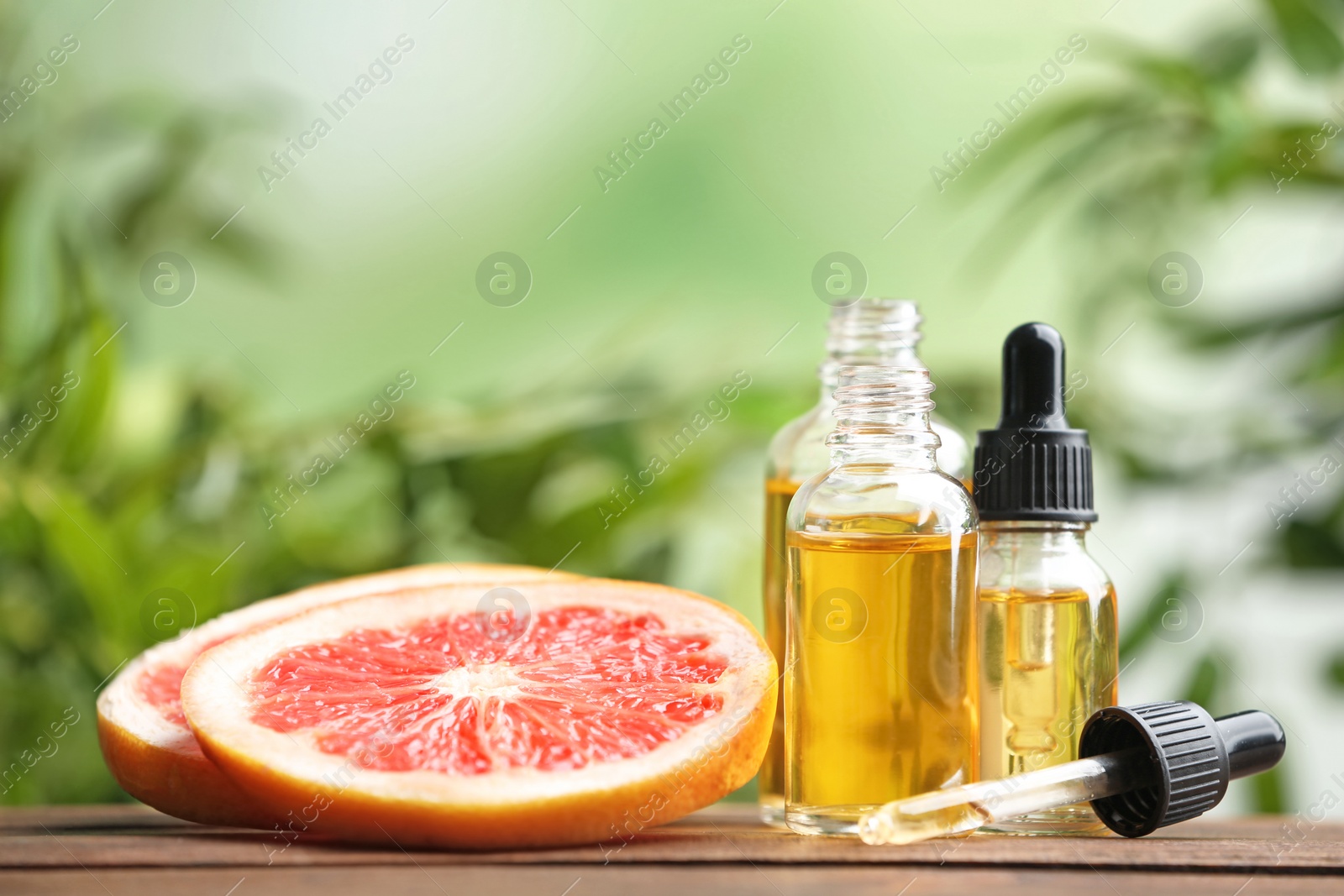 Photo of Bottles of essential oil and grapefruit slices on table against blurred background