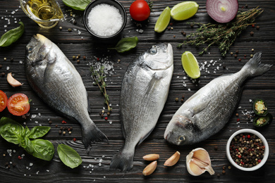 Flat lay composition with raw dorada fish on black wooden table