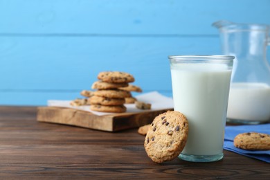 Photo of Delicious chocolate chip cookies and glass of milk on wooden table, space for text