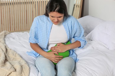 Young woman using hot water bottle to relieve cystitis pain on bed at home