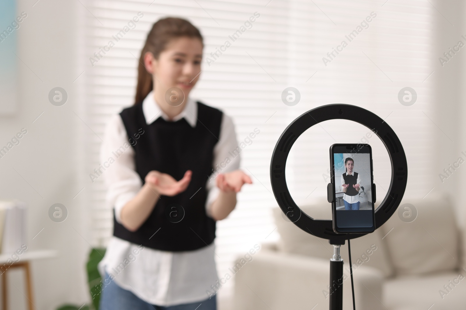 Photo of Teenage blogger explaining something while streaming at home, focus on smartphone