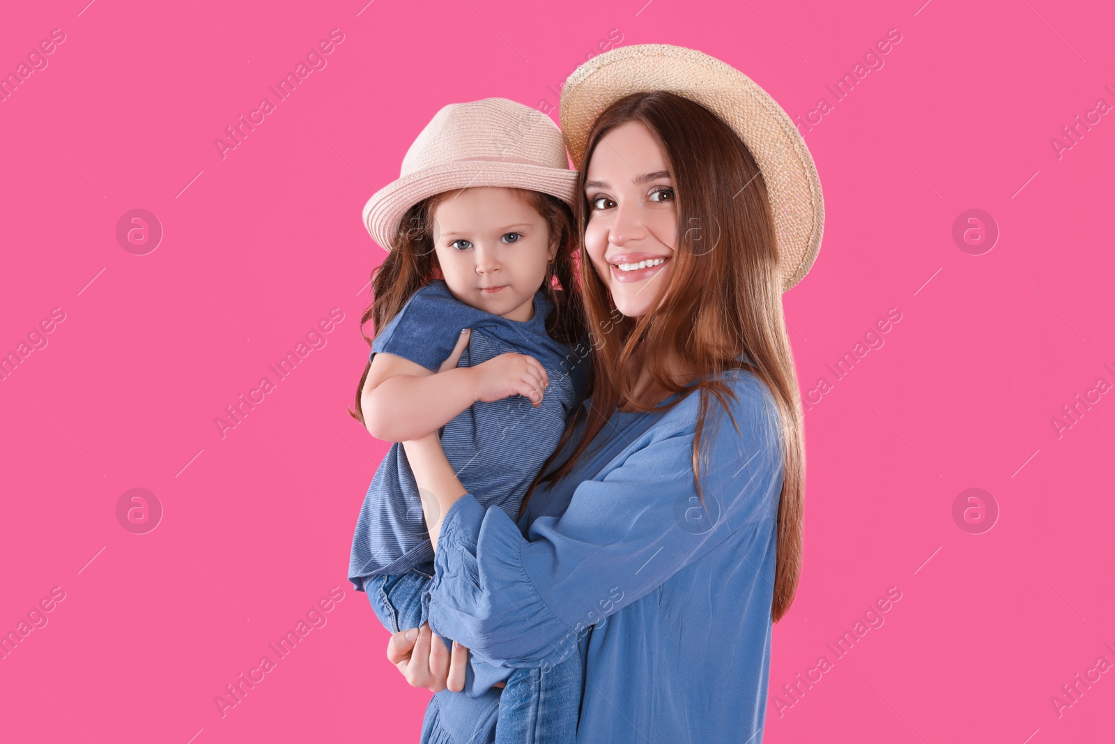 Photo of Young mother and little daughter with hats on pink background