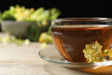 Cup of tea and linden blossom on wooden table, closeup. Space for text