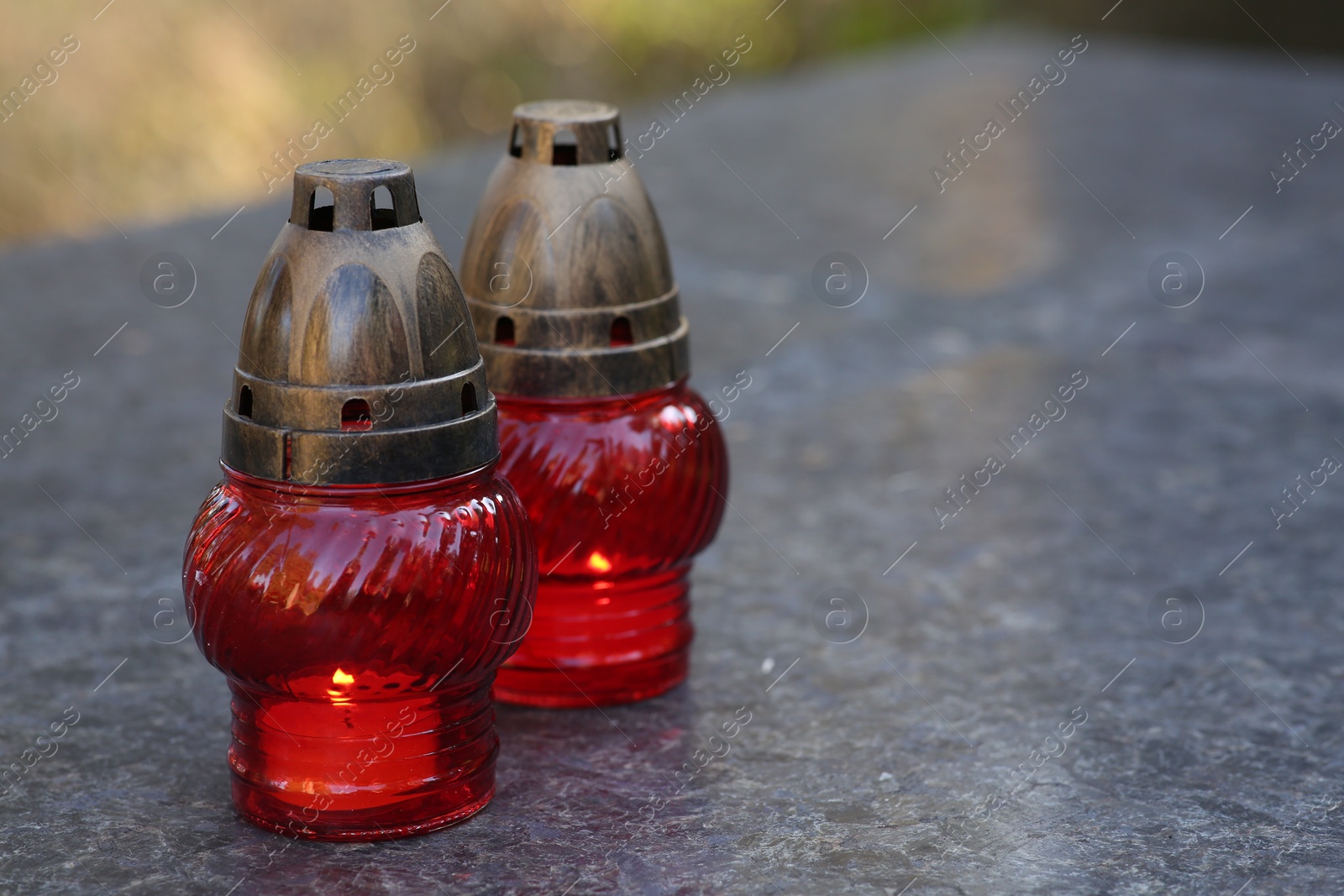 Photo of Red grave lanterns with burning candles on granite surface in cemetery, space for text