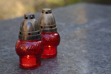 Photo of Red grave lanterns with burning candles on granite surface in cemetery, space for text