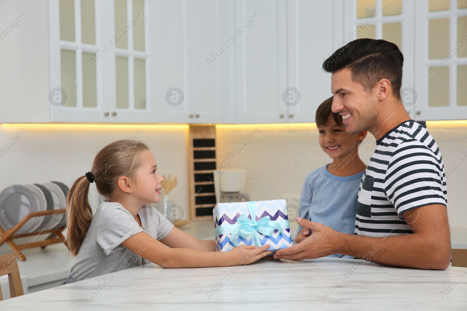 Photo of Man receiving gift for Father's Day from his children in kitchen